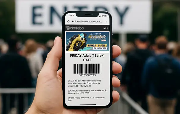 A person holds a smartphone displaying an electronic ticket with a QR code at an event ENTRY gate, with a blurred crowd queuing in the background